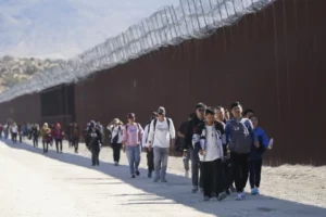 许多来自中国的非法移民在越过墨西哥边境寻求庇护后沿着隔离墙行走