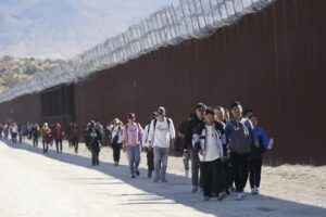 一群来自中国的非法移民越过墨西哥边境寻求庇护后沿着隔离墙行走